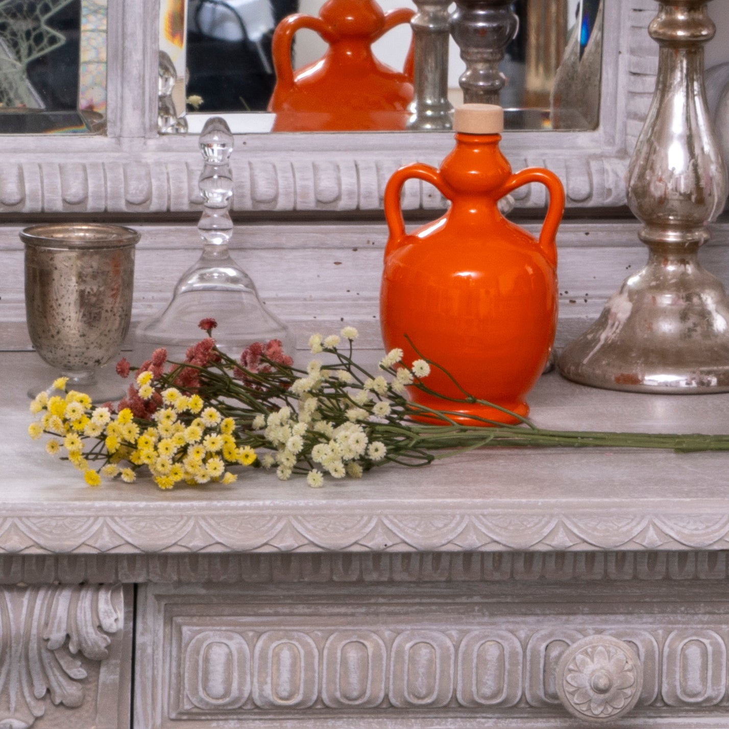Bottiglia arancione di Olio Extravergine di Oliva Coratina con fiori colorati su mobile decorativo
